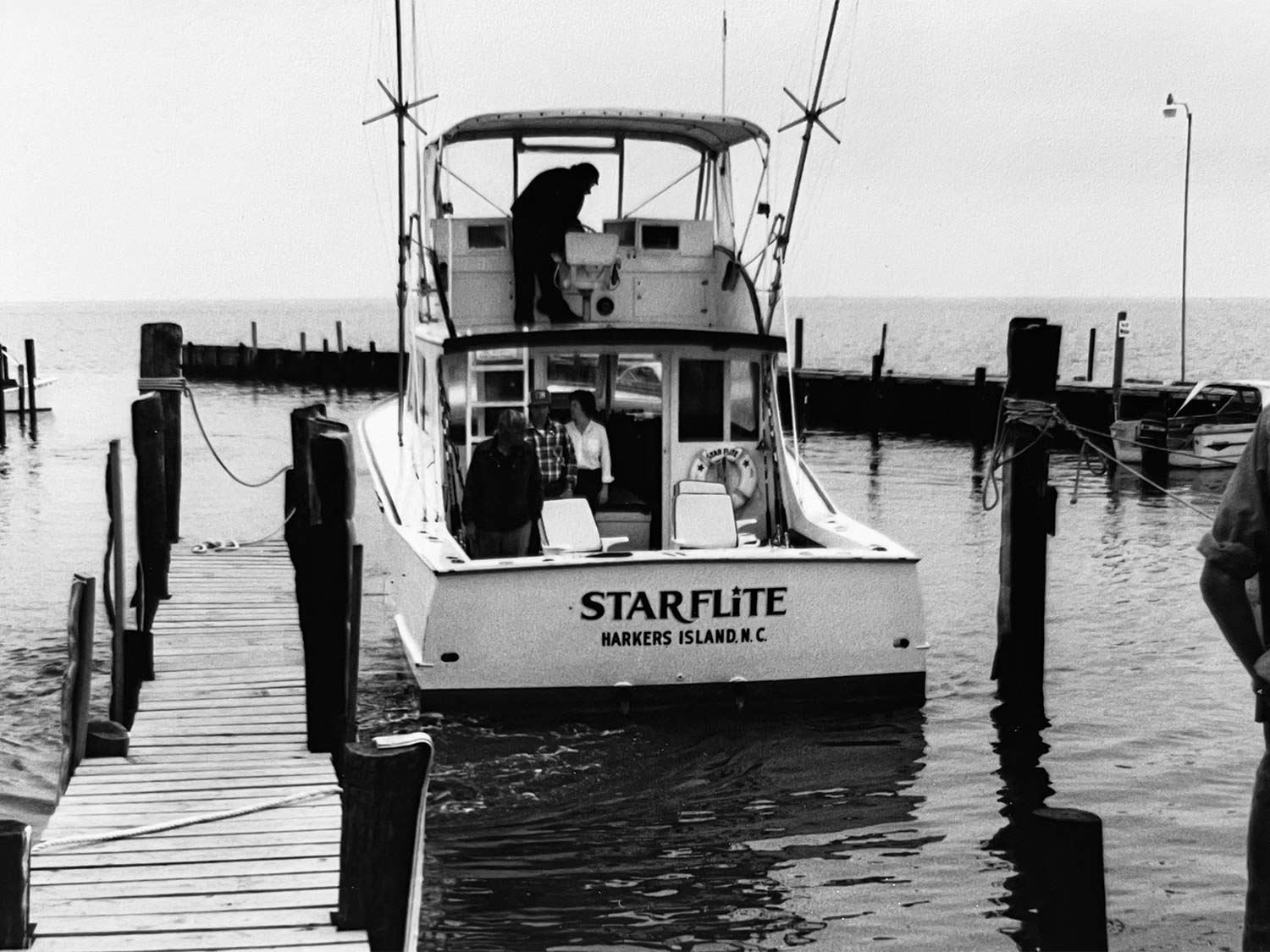 Black and white image of a small boat docked in a marina.